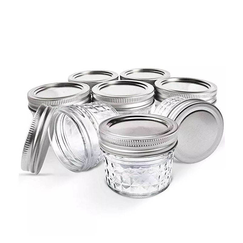 כמה מ-8 צנצנות זכוכית הברגה כפולה MASON JARS בנפח 118 מ"ל (4oz) עם מכסי מתכת מסודרים על רקע לבן, חלקם עומדים זקופים ואחרים מוטים או שוכבים. כמה מ-8 צנצנות זכוכית הברגה כפולה MASON JARS בנפח 118 מ"ל (4oz) עם מכסי מתכת מסודרים על רקע לבן, חלקם עומדים זקופים ואחרים מוטים או שוכבים.