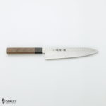 סכין שף יפנית Gyuto רב תכליתית עם ידית עץ ולהב נירוסטה 45 שכבות דמשק AUS10. הוא כולל דמויות חרוטות, ממותגות "סאקורה" בפינה השמאלית התחתונה.