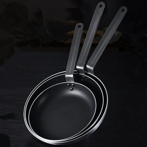 שלוש מחבתות אלומיניום עם ציפוי טפלון NON STICK בגדלים שונים עם ידיות מתכת ארוכות מונחות זו על גבי זו על משטח כהה.
