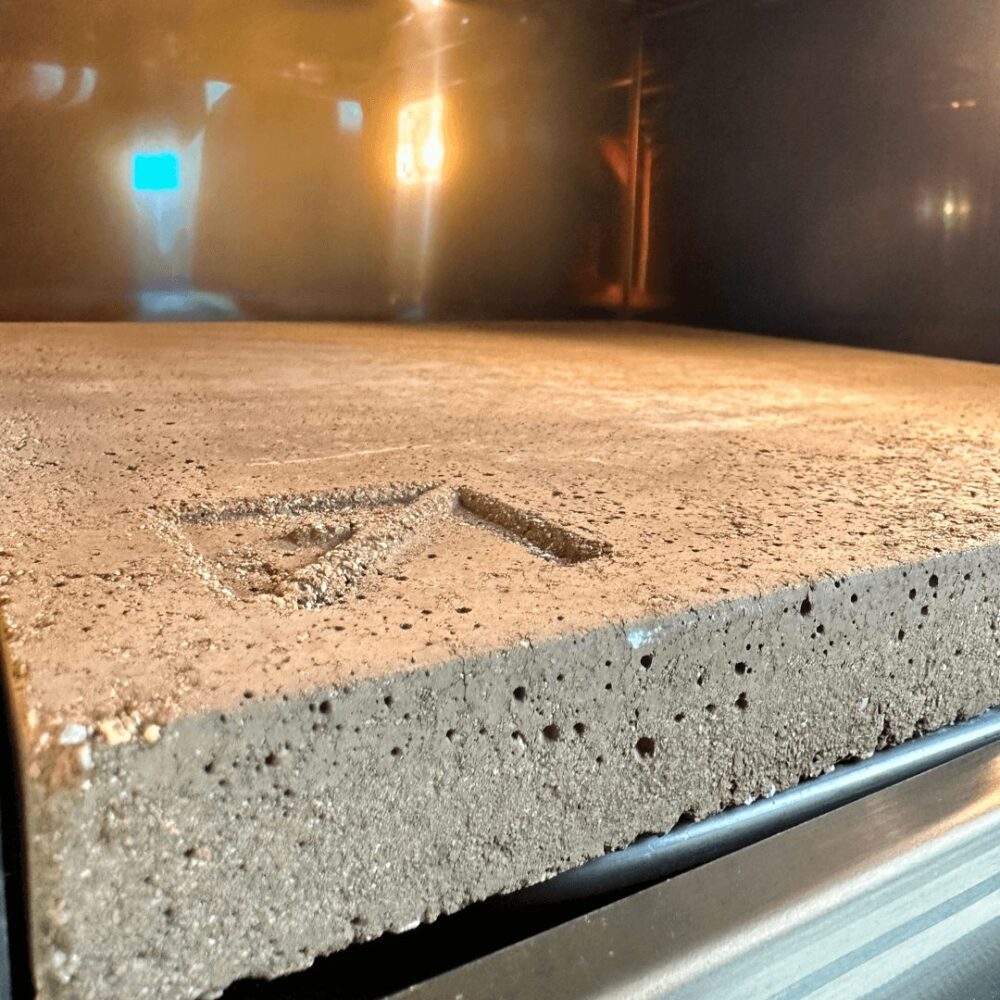 תקריב של אבן אפייה מלבנית ונקבובית עם סימון משולש בתוך EFFEUNO P134H 509E תנור פיצה Extra Power, מוארת באור.