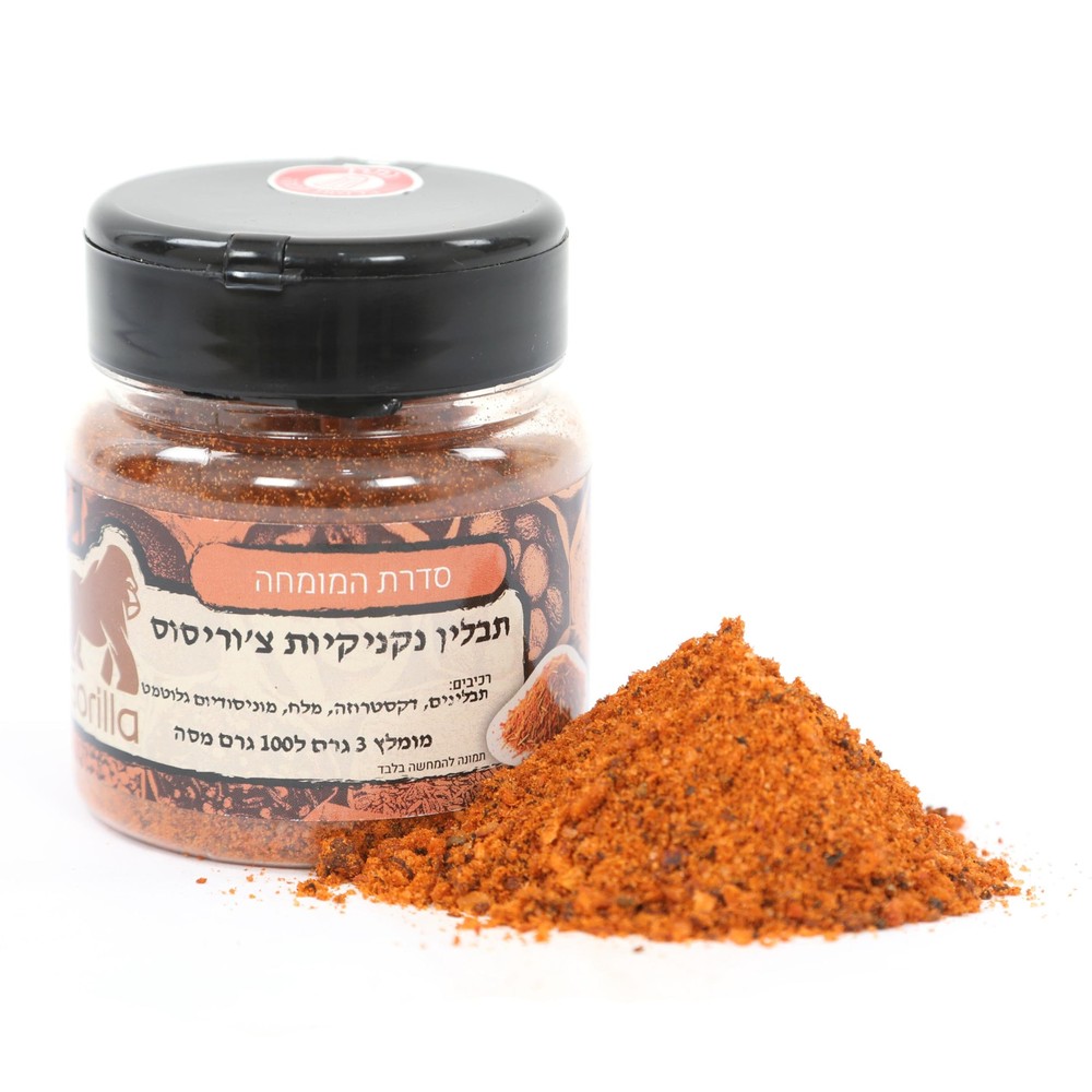 צנצנת של תערובת תבלינים בצבע כתום-אדמדם עם כיתוב בעברית על התווית, לצד ערימה קטנה של התבלין בתפזורת על רקע לבן.